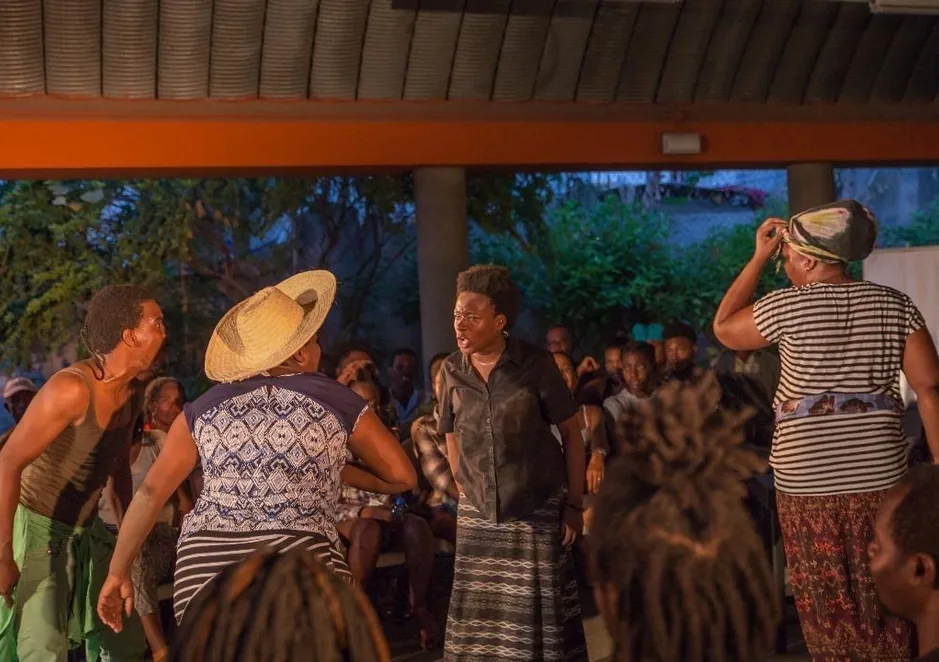 An evening performance under a canopy: women in straw hats and striped skirts before a crowd