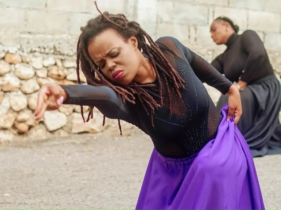 A dancer in a black top and purple skirt bending low, arm outstretched