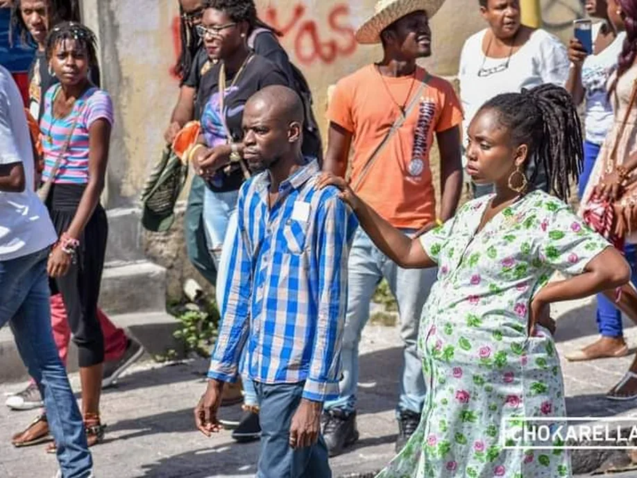 A street scene: a pregnant woman in a floral dress beside a man in a checked shirt, a crowd behind them
