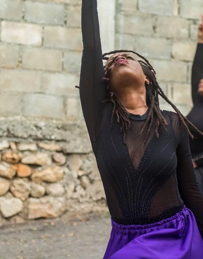 A dancer in black reaching one arm high, eyes closed