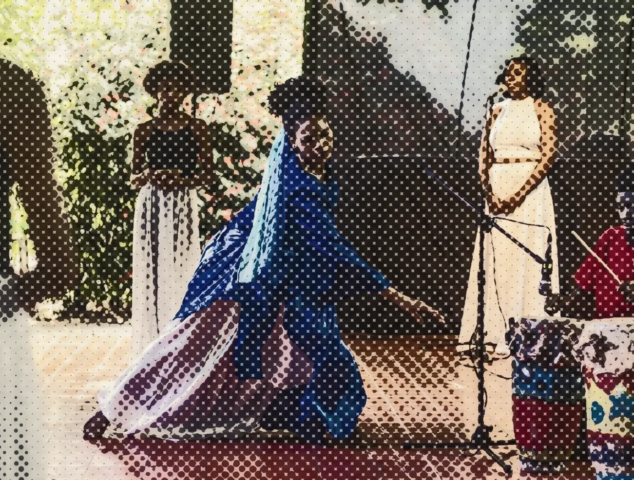 A dancer in blue beside drummers on a tiled stage