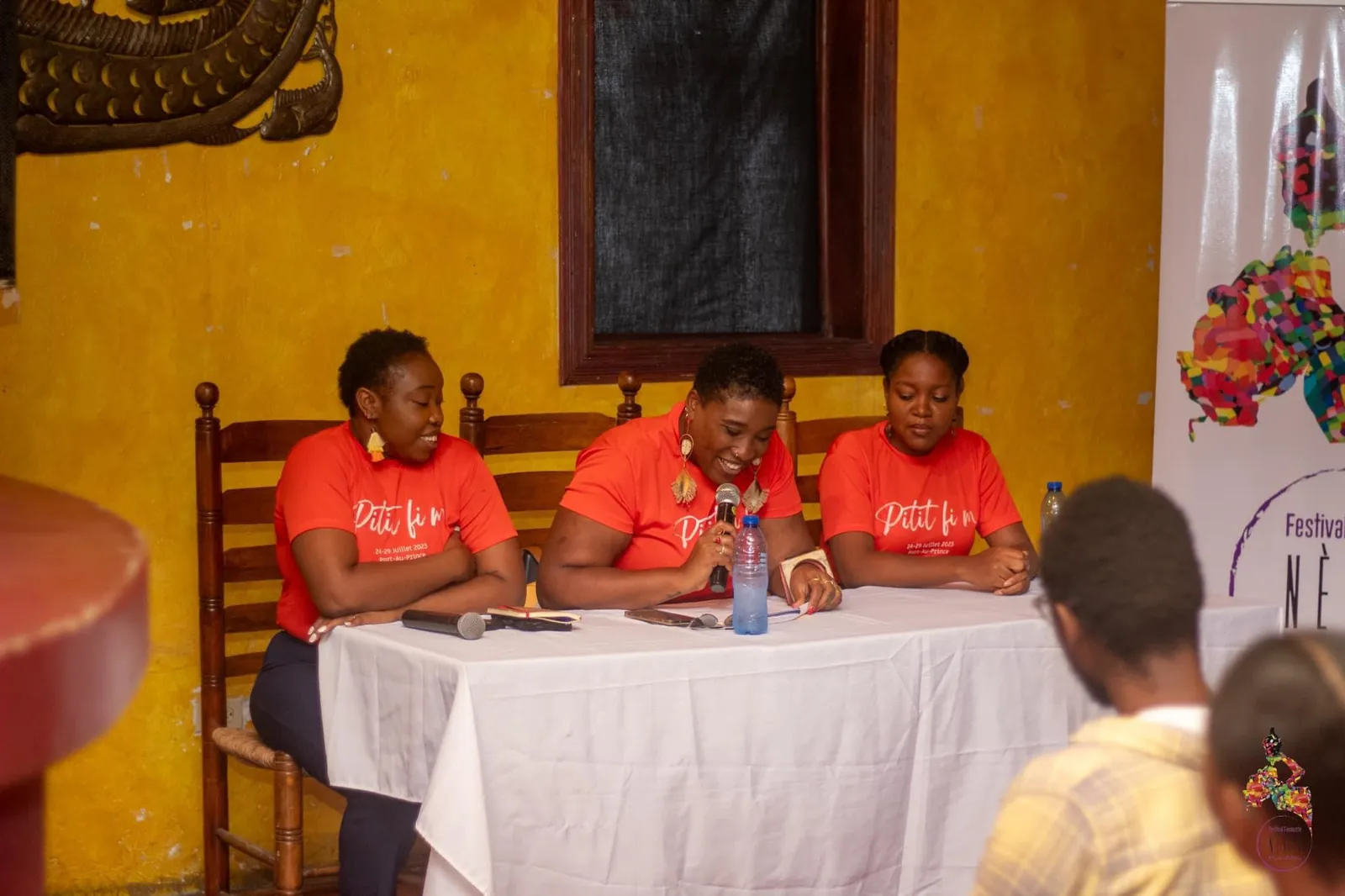 Three women in red festival T-shirts at a panel table