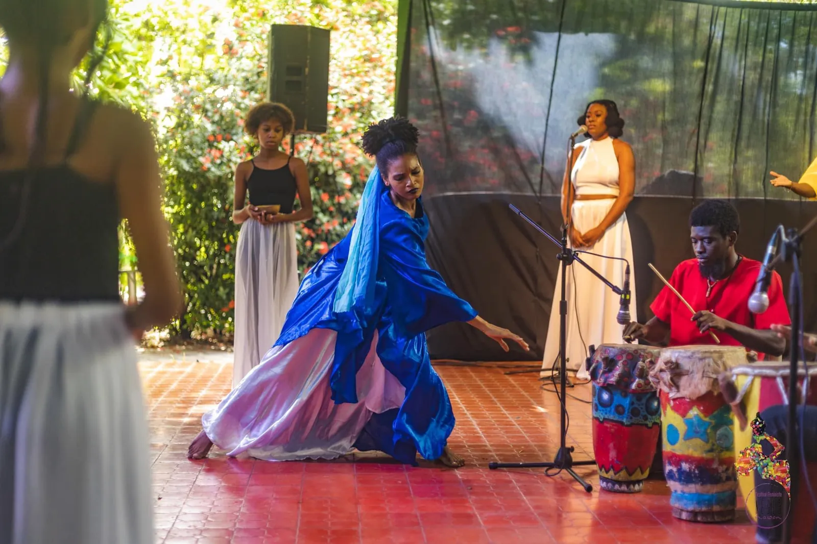 A dancer in blue beside drummers on a tiled stage